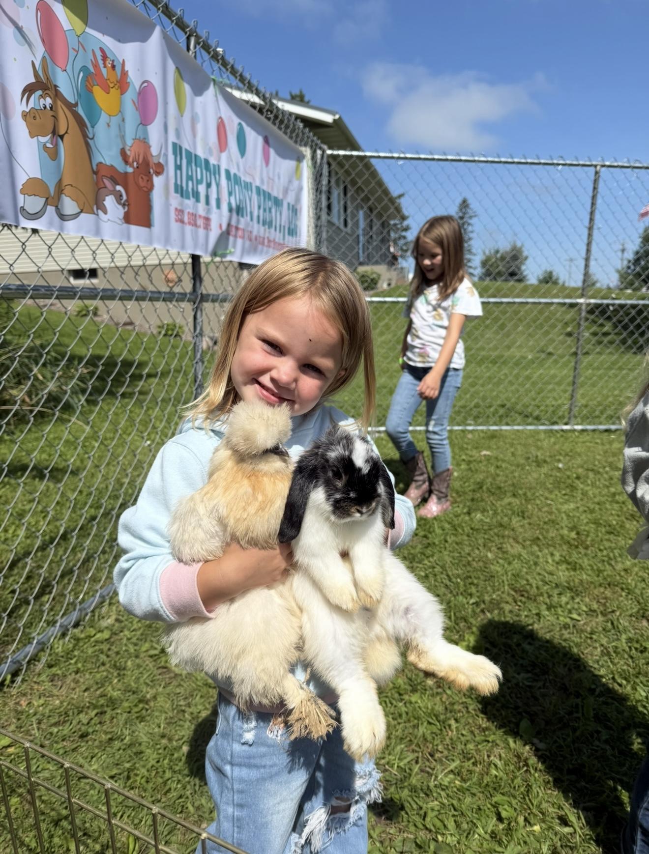 A girl holding a silkie chicken and a lop-eared rabbit at a Pony Parties Express event