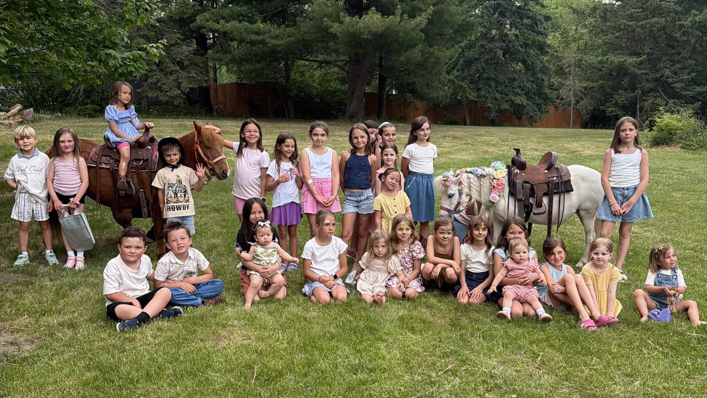 A large group of children gathered with two Pony Parties Express ponies at a group event