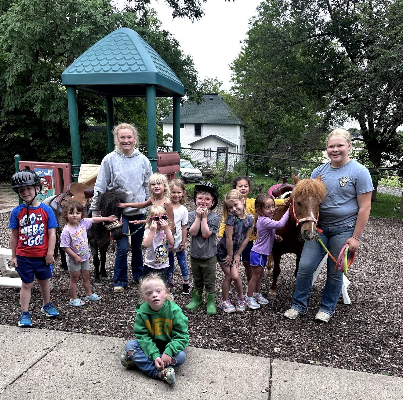 Two ponies visiting a playground with a group of children