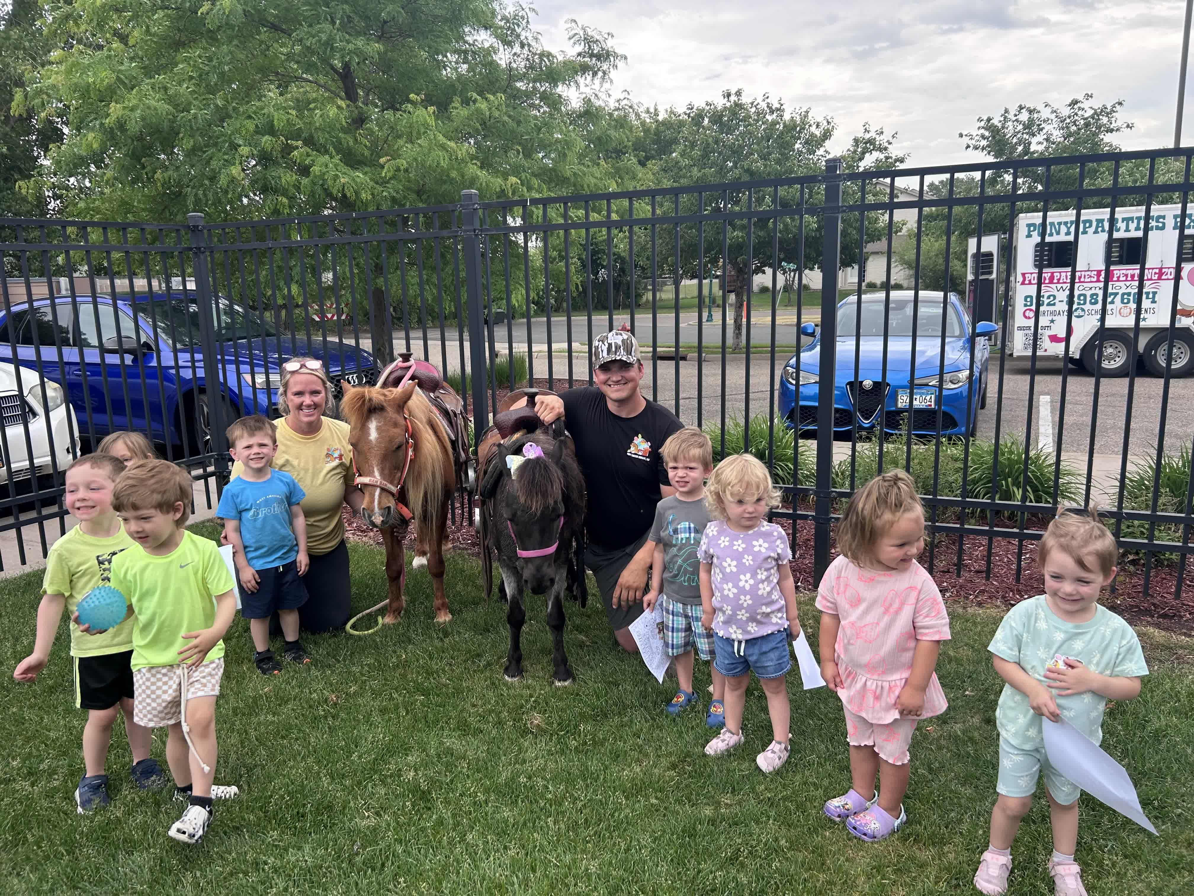 Kyle and Krista Knops with two ponies greeting young guests, the Pony Parties Express trailer behind