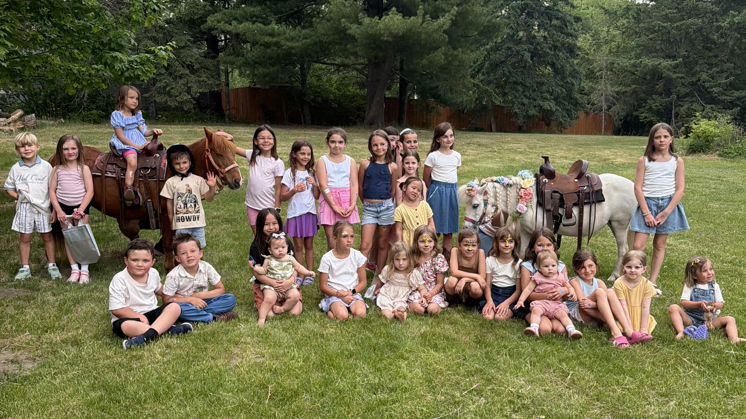 A large group of children gathered with two Pony Parties Express ponies at a group event