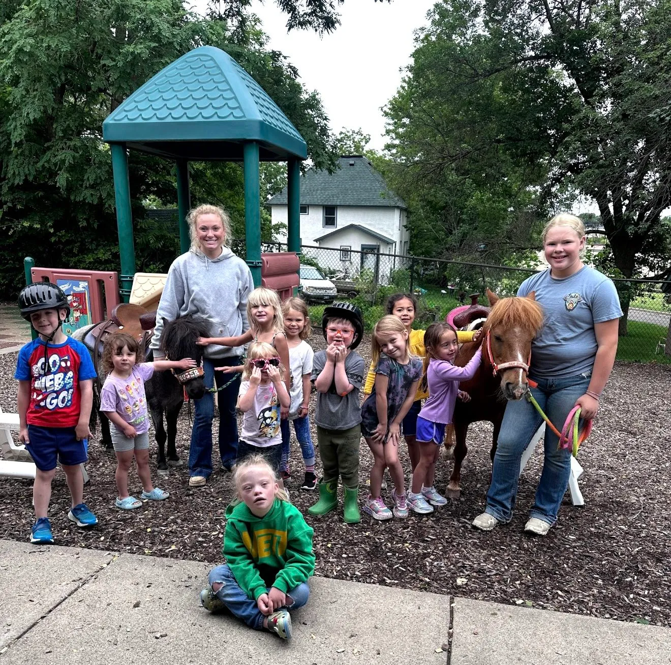 Two ponies visiting a playground with a group of children