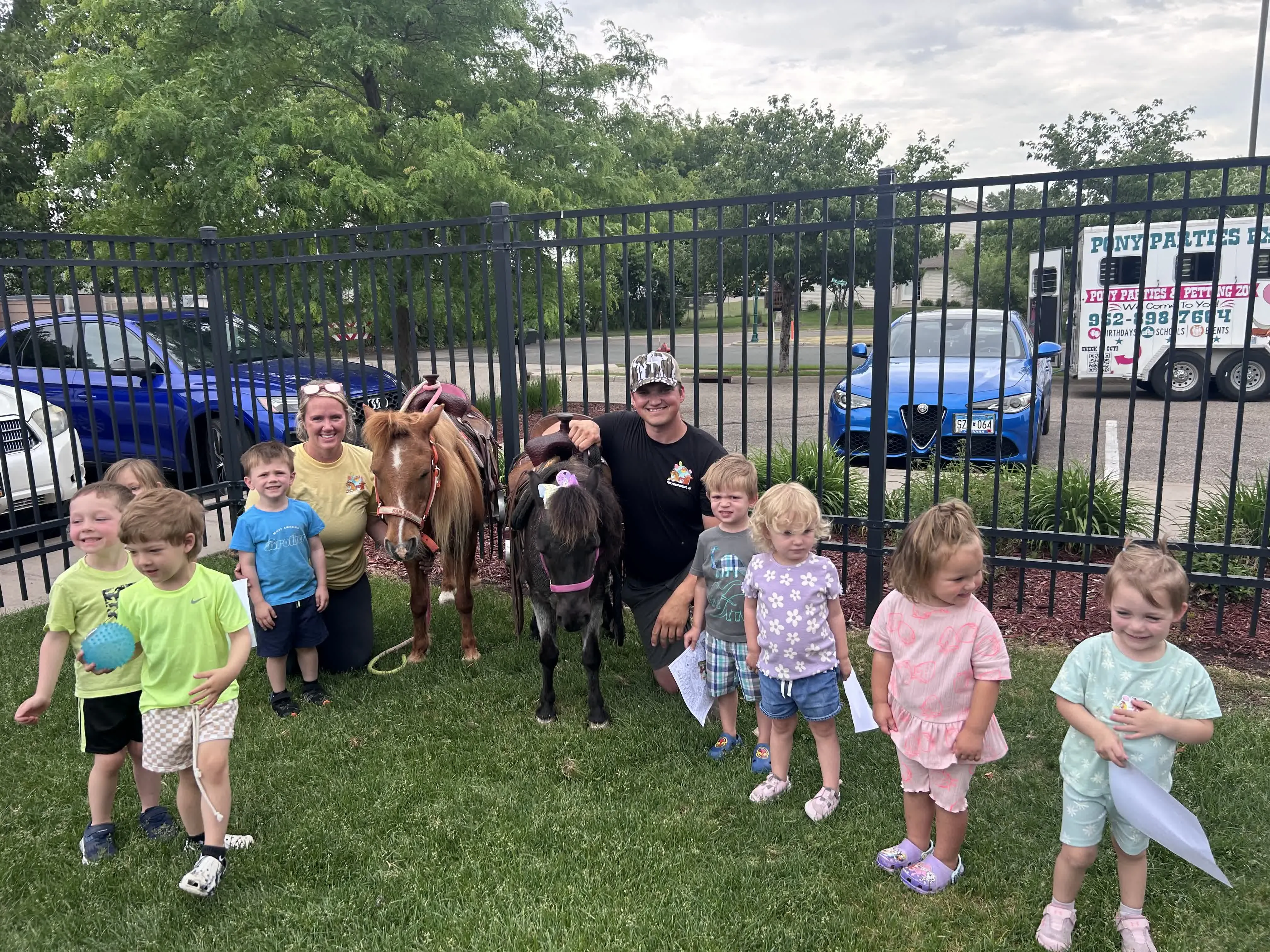 Kyle and Krista Knops with two ponies greeting young guests, the Pony Parties Express trailer behind