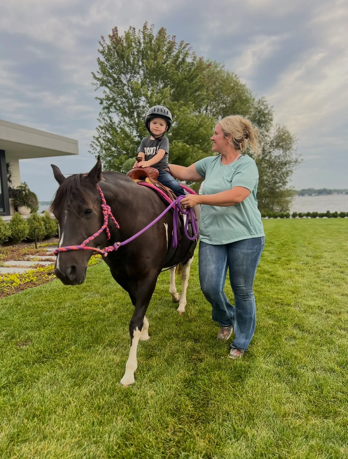 A toddler on a first pony ride, led by a handler across a backyard